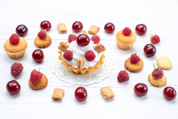 Top view yummy little cakes with raspberries and cream along with cookies and cakes on the light table cake biscuit sweet berry fruit