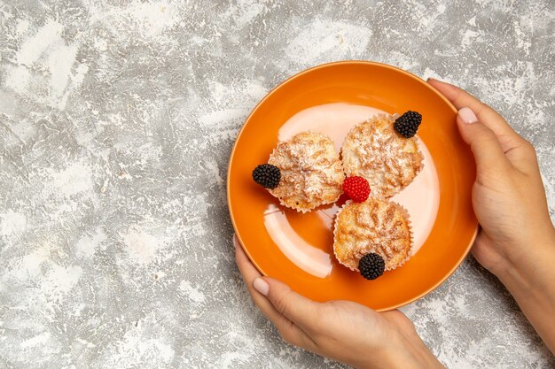 Вид сверху вкусные маленькие пирожные с сахарной пудрой на белом фоне