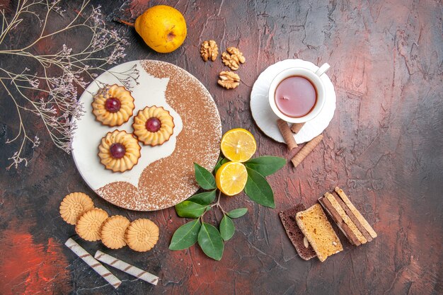 Top view yummy little cookies with cup of tea on the dark table sugar cake sweet biscuit