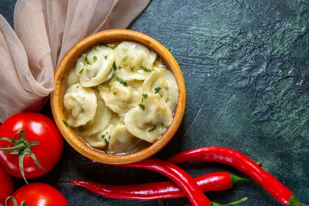 Top view yummy meat dumplings inside wooden plate with fresh tomatoes on dark surface