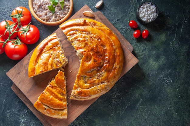 Top view of yummy meat pie with red tomatoes on dark surface