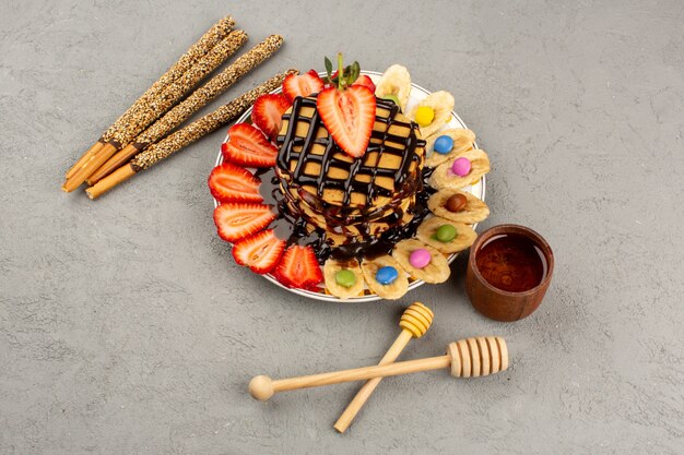상위 뷰 맛있는 팬케이크 초콜렛 팬케이크 빨간 얇게 썬 딸기와 바나나 회색 배경에 흰색 접시 안에