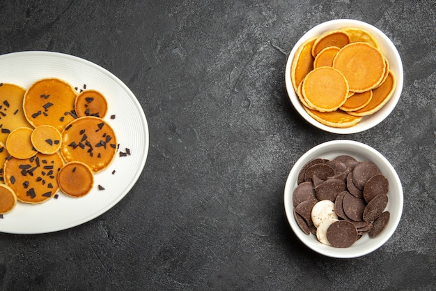 Вид сверху вкусные блины с шоколадными чипсами и печеньем на темном фоне