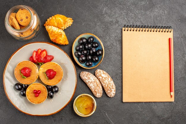 Top view yummy pancakes with fruits and cakes on dark