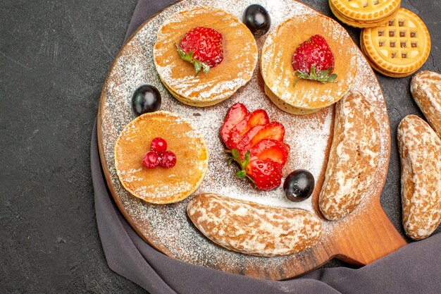 Top view yummy pancakes with fruits and sweet cakes on dark desk