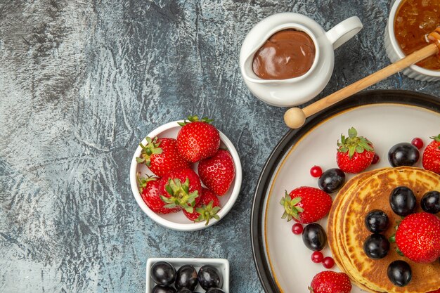 Top view yummy pancakes with honey and fruits on light