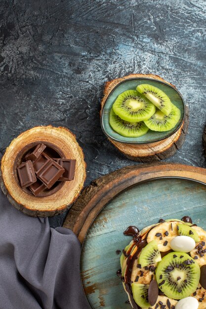 Вид сверху вкусные блины с нарезанными фруктами и шоколадом на темно-серой поверхности сладкого цвета завтрак сахарный фруктовый торт десерт