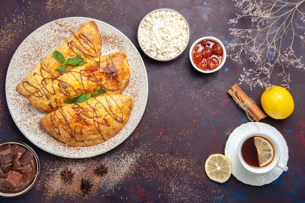 暗い背景のペストリー甘い焼き茶ケーキシュガークッキーにお茶とカッテージチーズのカップとおいしいペストリーの上面図