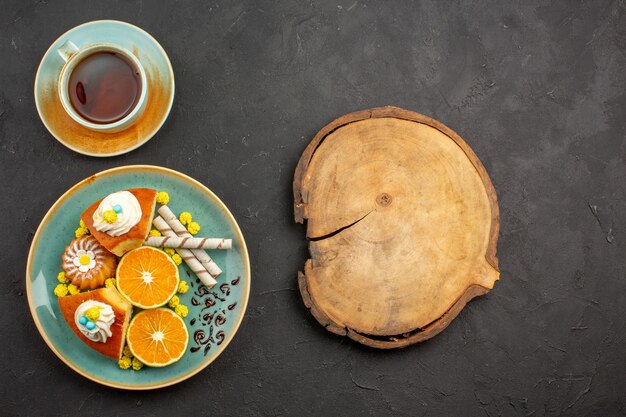 Foto gratuita vista dall'alto gustose fette di torta con mandarini freschi e tazza di tè al buio