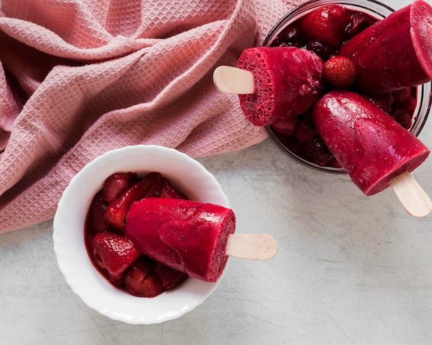 Top view of yummy popsicles in cup and jar with strawberries