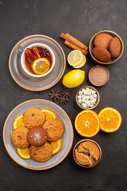 Top view yummy sand cookies with fresh oranges and cup of tea on dark background fruits biscuit sweet cookies citrus sugar