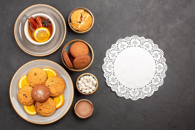 Top view yummy sand cookies with oranges and cup of tea on dark background biscuit fruit citrus sweet cake cookie