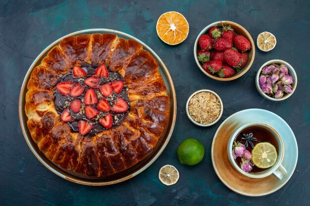 Top view of yummy strawberry pie baked delicious cake with cup of tea on dark-blue surface