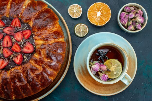 Top view of yummy strawberry pie baked delicious cake with cup of tea on dark-blue surface