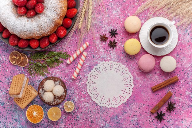 Вид сверху вкусный клубничный пирог с французскими макаронами и чашкой чая на розовом