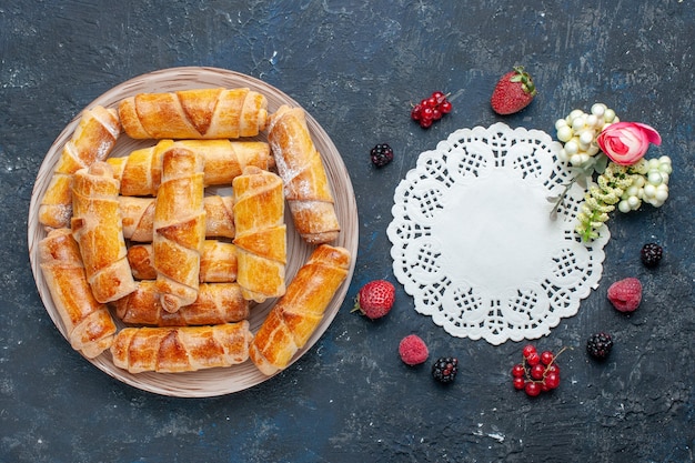 Top view yummy sweet bangles with filling inside plate along with berries on the dark desk sweet biscuit cake bake pastry