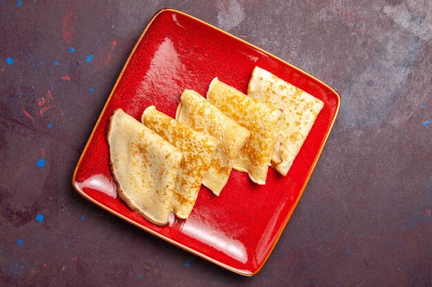 Top view of yummy sweet pancakes inside red plate on dark