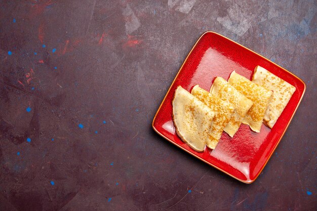 Top view of yummy sweet pancakes inside red plate on dark