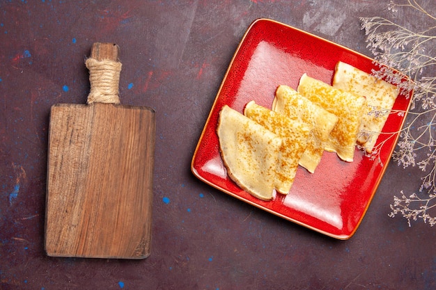 Top view of yummy sweet pancakes inside red plate on dark