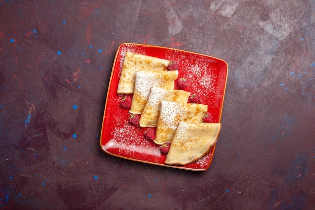 黒いテーブルの上のラズベリーと赤いプレートの内側のおいしい甘いパンケーキの上面図