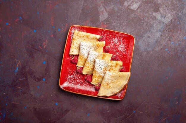 Top view of yummy sweet pancakes inside red plate with raspberries on black table