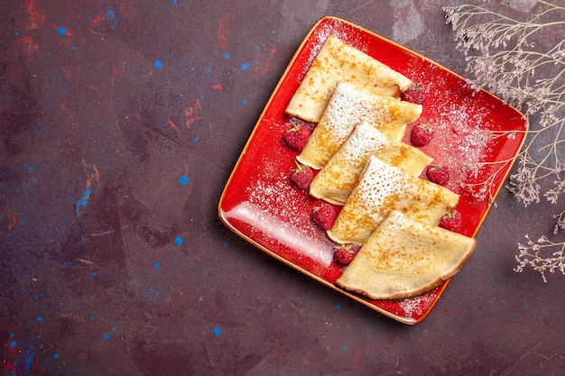 Top view of yummy sweet pancakes inside red plate with raspberries on black