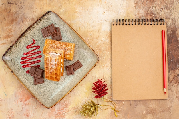 Вид сверху вкусные вафельные коржи с шоколадными батончиками на коричневом фоне