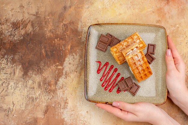 Вид сверху вкусные вафельные коржи с шоколадными батончиками на коричневом фоне