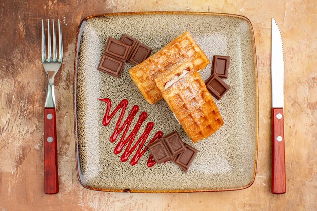 Top view yummy waffle cakes with chocolate bars on the brown background