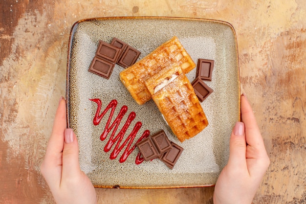 Top view yummy waffle cakes with chocolate bars on the brown background