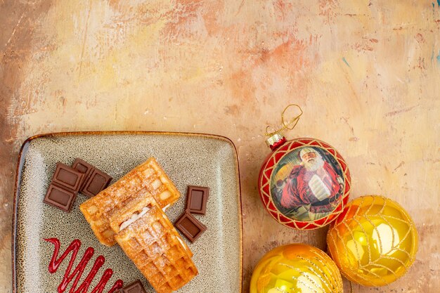 Top view yummy waffle cakes with chocolate and new year tree toys on a light background