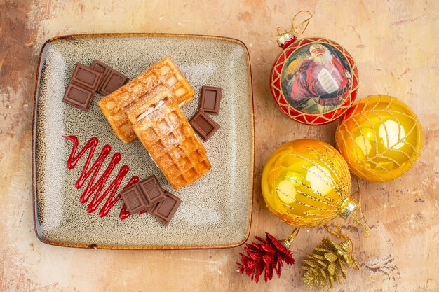 Top view yummy waffle cakes with chocolate and new year tree toys on light background