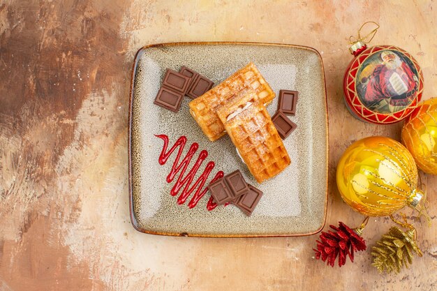 Top view yummy waffle cakes with chocolate and new year tree toys on the light background