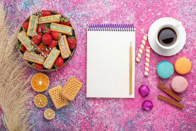 Vista dall'alto di deliziosi biscotti waffle con macarons francesi e fragole rosse fresche sulla superficie rosa