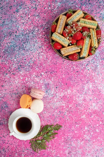 Вид сверху вкусного вафельного печенья со свежей красной клубникой и чаем на розовой поверхности