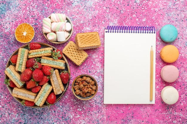 Foto gratuita vista dall'alto di deliziosi biscotti waffle con macarons e fragole rosse fresche sulla superficie rosa