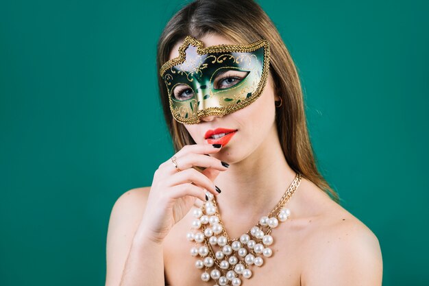 Topless woman wearing masquerade carnival mask and necklace on green backdrop