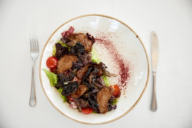 Topview of served beef salad with a cherry tomatos and lettuce on the white table