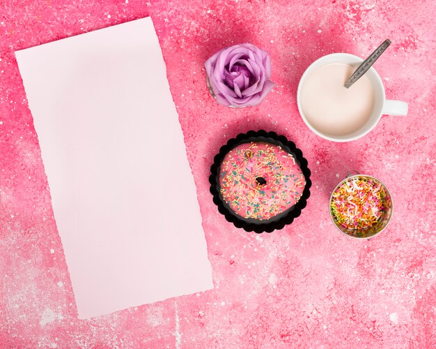 Torn blank white paper with sprinkles; donut; rose and milk against pink textured backdrop