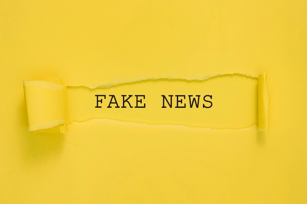 Torn fake news paper on yellow wall