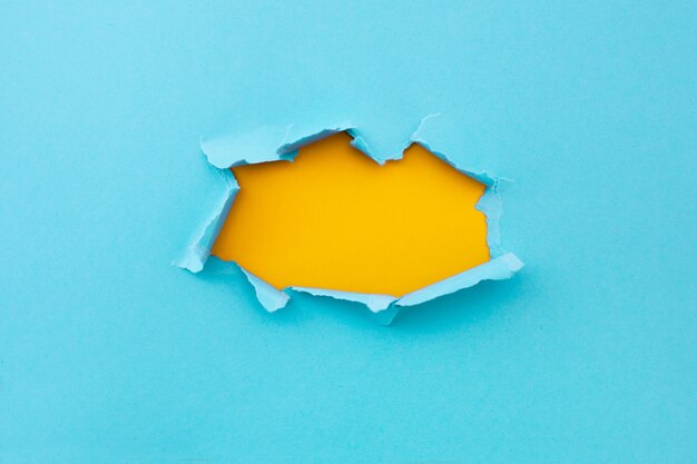 Torn hole in blue color and ripped of paper with yellow background. Torn paper texture with copy space area for text 