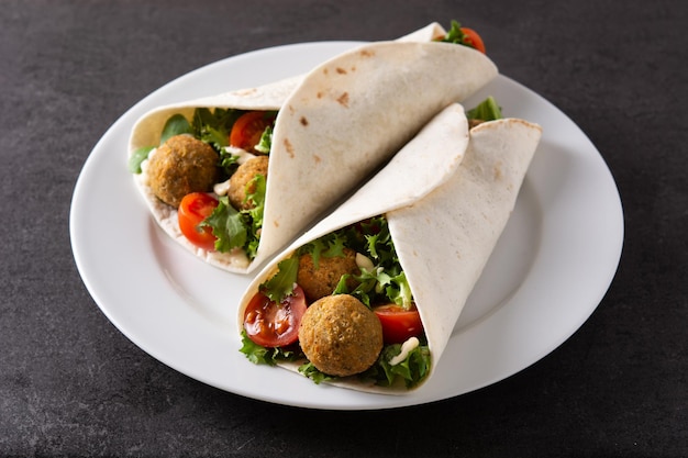 Tortilla wrap with falafel and vegetables on black stone background