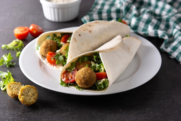 Tortilla wrap with falafel and vegetables on black stone background
