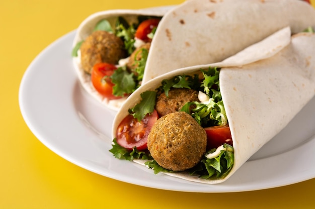 Tortilla wrap with falafel and vegetables on yellow background