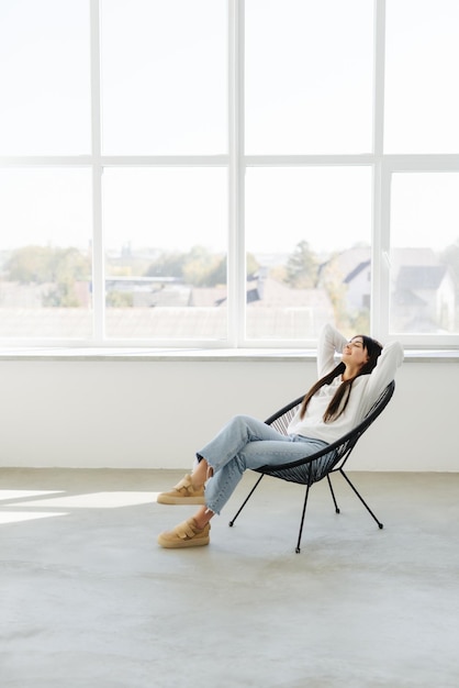 Free photo total relaxation attractive young woman holding hands behind head and smiling while sitting at the chair at home