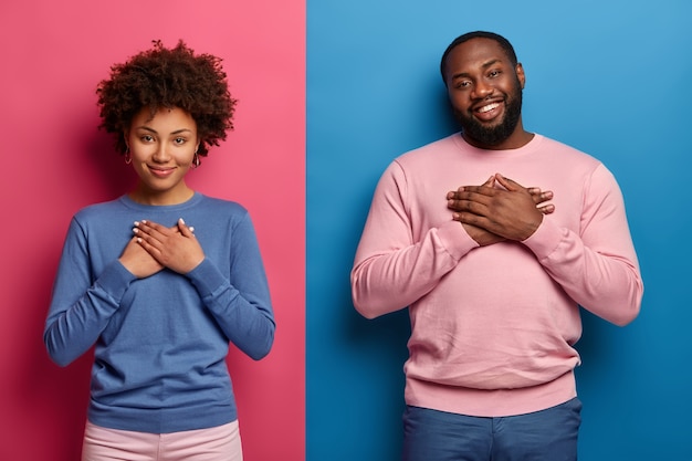 Foto gratuita la sorella e il fratello dalla pelle scura, toccati, apprezzano la cura dei genitori, il sostegno costante, tengono i palmi delle mani sul cuore, esprimono gratitudine e sentimenti calorosi