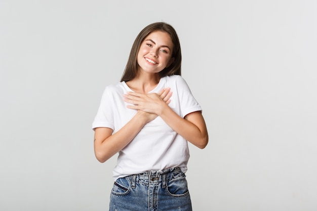 Touched happy young woman smiling, holding hands on chest, feeling thankful.