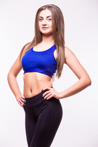 Tough young woman standing on grey background. Muscular female looking at camera. Female bodybuilder wearing gloves ready for gym exercise.