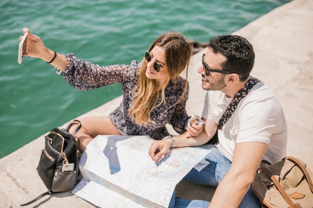 Tourist couple sitting on jetty talking self portrait on mobile phone