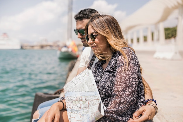 Tourist couple sitting together on jetty with map